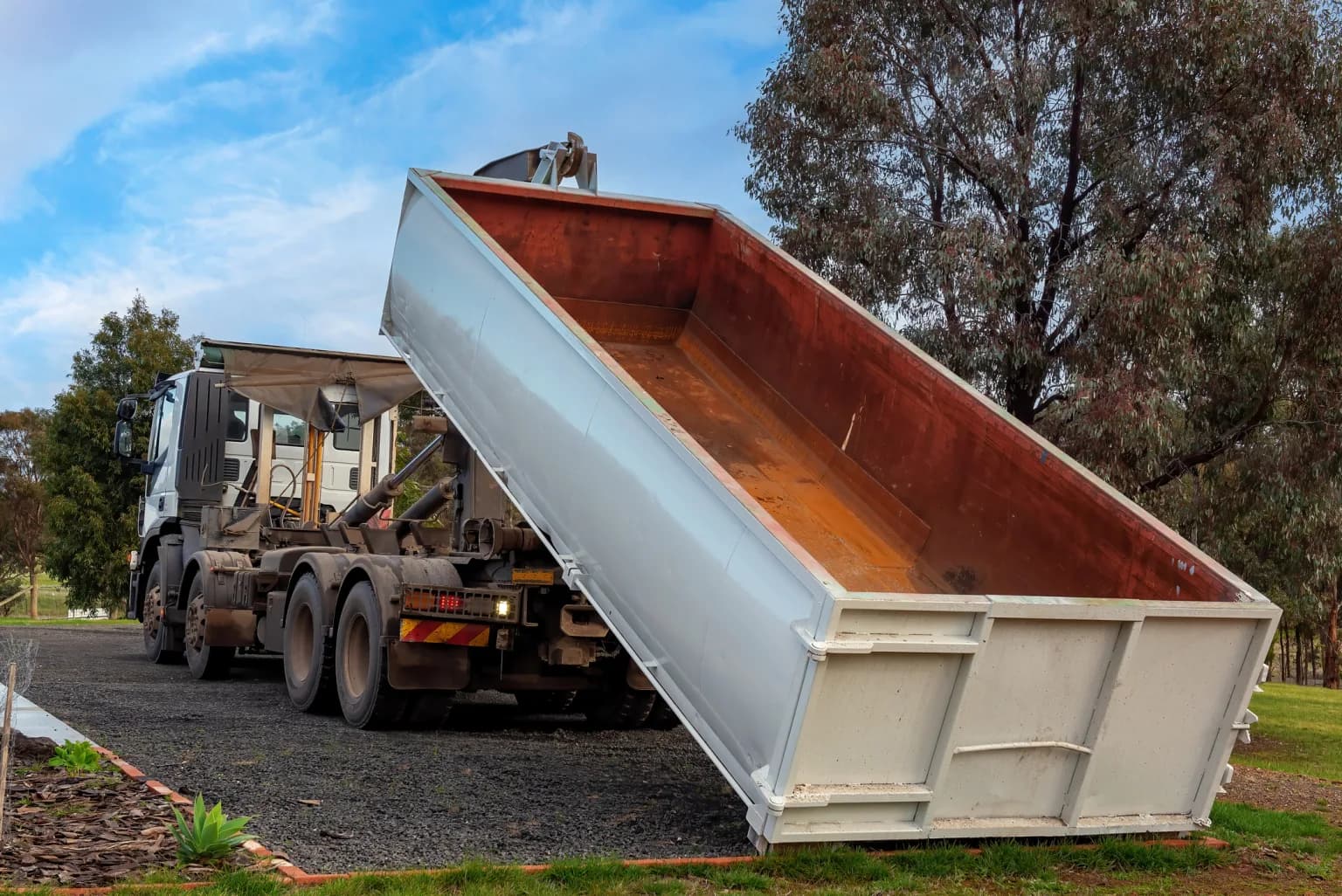 A truck tipping an empty steel container onto a gravel drive